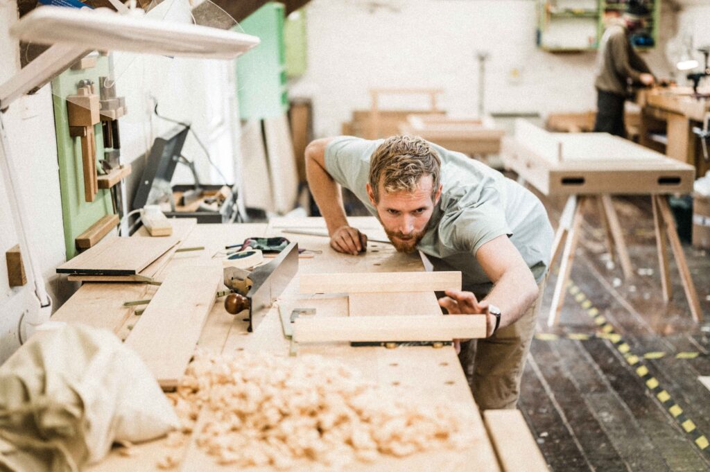 A STUDENT AT ROWDEN ATELIER ON A FINE WOODWORKING COURSE, CHECKING COMPONENTS WITH WINDING STICKS FOR TWIST.